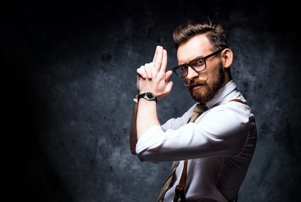 Young stylish bearded man in glasses posing with a finger gun.